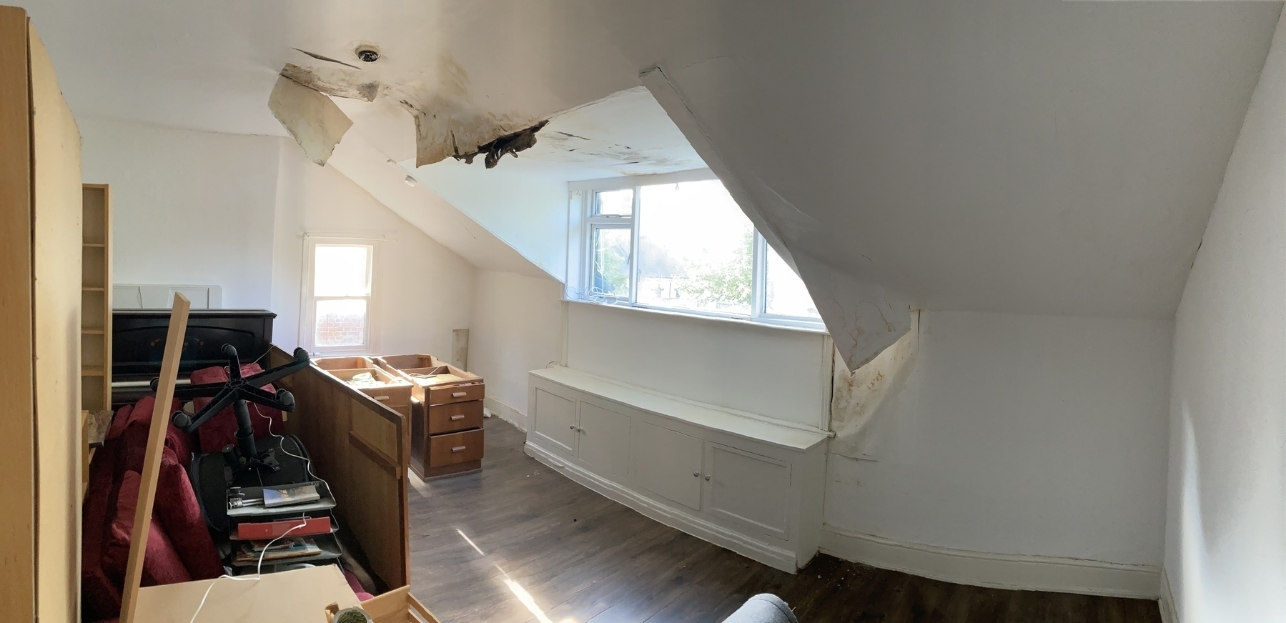 A room with water damaged ceiling, the furniture piled on one side, awaiting repairs.&10;