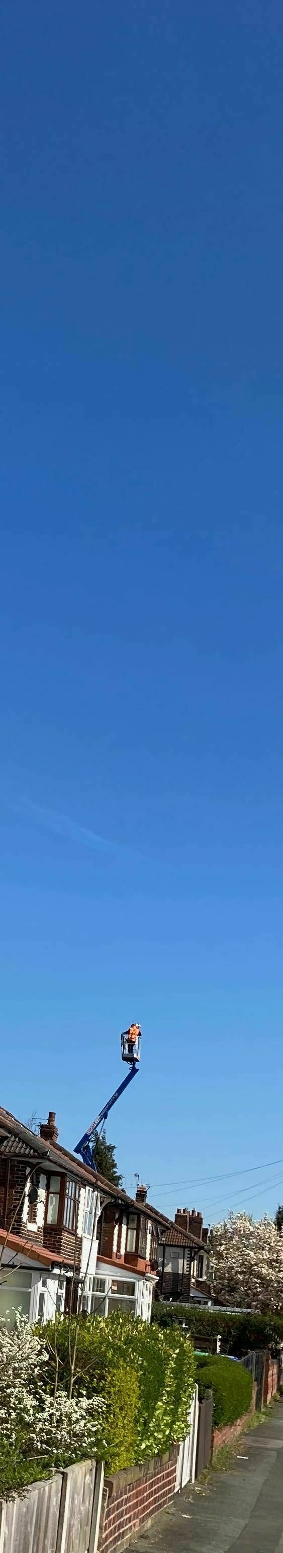 Above the roofs of a suburban street a person stands on an elevated platform beneath an expanse of blue sky.