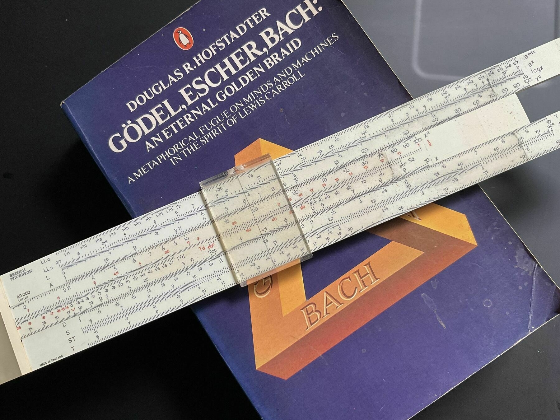 A slide rule lays across the book Godel, Escher, Bach.